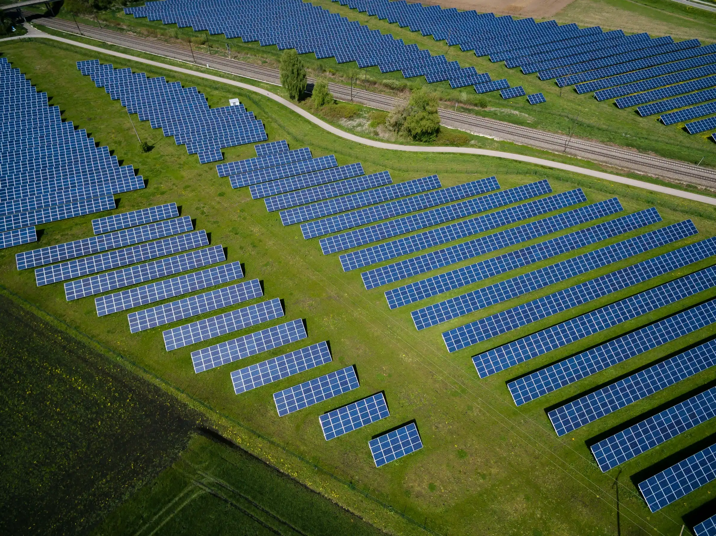 Aerial view of a ground-mounted solar farm with rows of panels on green grass