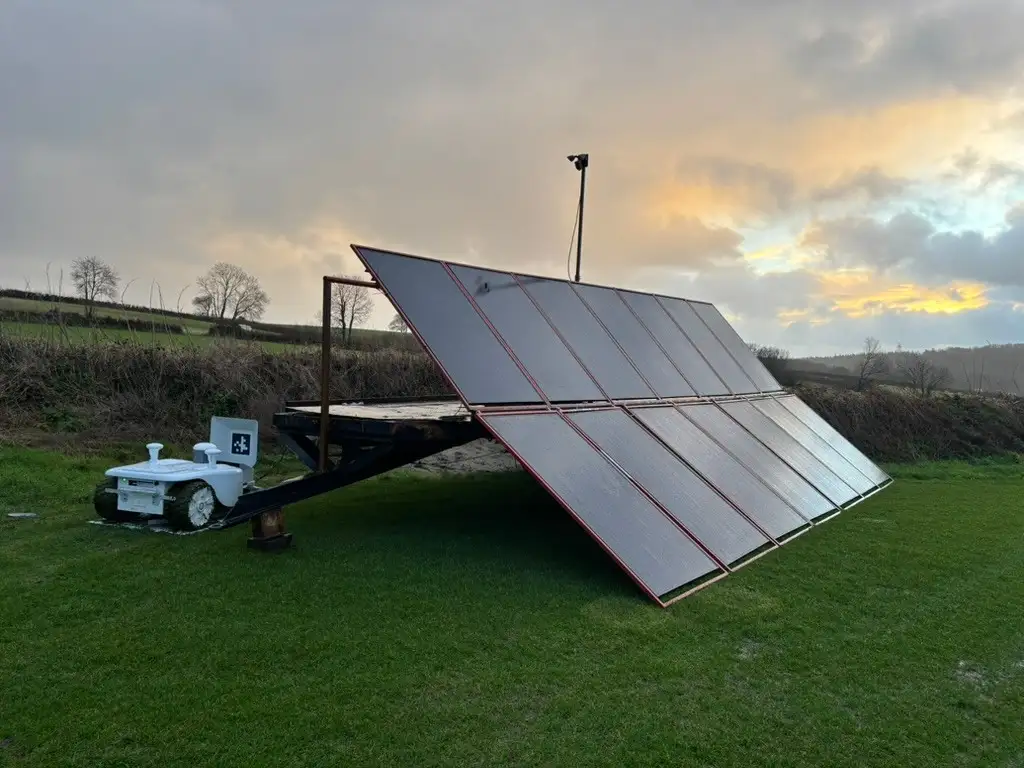 Solar panel trailer in a green field charging a white autonomous lawnmower, built by Quanta