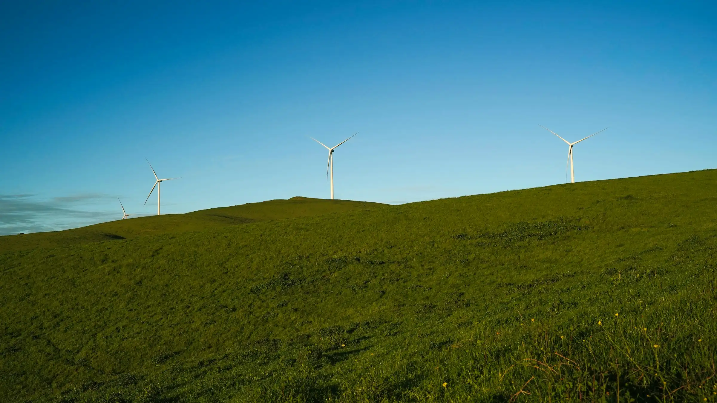 Three wind turbines on a green hill under a blue sky